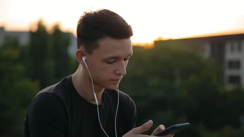 Handsome young man in earphones using phone at sunset outdoors 1 Stock Footage 94621902