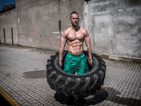 Handsome young man exercising flipping huge tire Stock Photos