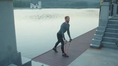 Handsome young man exercising with trx suspension strap near lake crossfit Stock Footage 138654141