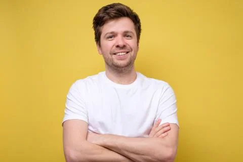 Handsome young man with folded hands smiling against yellow background Stock Photos