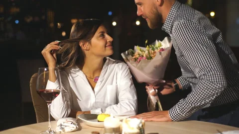 Handsome young man giving present and flowers to beautiful woman in cafe Stock Footage 91194704