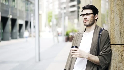 Handsome young man in glasses drinking coffee and waiting in the street Stock Footage