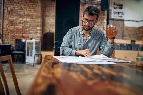Handsome young man with glasses holding drink and reading newspaper in mode.. Stock Photos