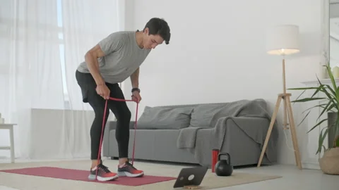 Handsome Young Man in a Gray T-Shirt and Black Shorts Does Sports at Home Online Stock Footage 134909961