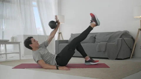 Handsome Young Man in a Gray T-Shirt and Black Shorts Does Sports at Home Online Видео 134911401