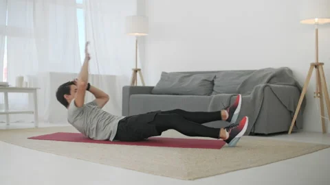 Handsome Young Man in a Gray T-Shirt and Black Shorts Does Sports at Home Online Vídeos de archivo 134911883