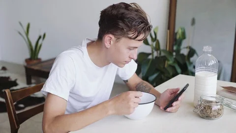 Handsome young man has breakfast cereal and looks at phone Stock Footage 79829720