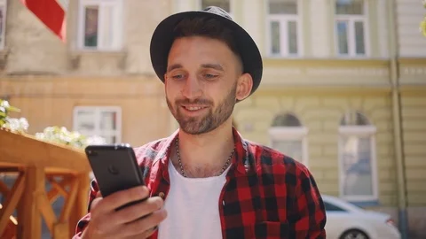 Handsome young man in the hat uses phone walk in city smile feel happy blurred Stock Footage 92070050
