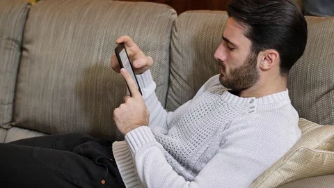 Handsome young man at home reading with ebook reader Video stock 83864249