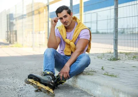Handsome young man with inline roller skates sitting on curb outdoors Stock Photos