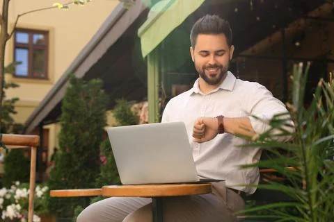Handsome young man with laptop checking time on watch at table in outdoor c.. Stock Photos
