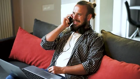 Handsome young man laughing while taking a phone call in his living room. Stock Footage 136547693