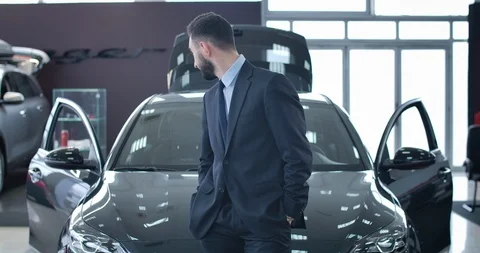 Handsome young man looking back at new black car, turning to camera and smiling Stock Footage 124402221