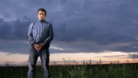 Handsome young man looking at the camera at sunset on the field. Beautiful sky Video stock 76949516