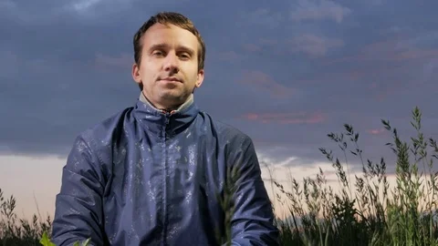 Handsome young man looking at the camera at sunset on the field. Beautiful sky Stock Footage 76951436