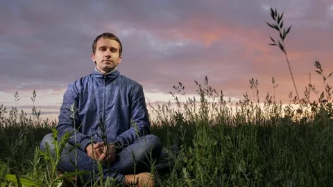 Handsome young man looking at the camera at sunset on the field. Beautiful sky Stock Footage 76971095