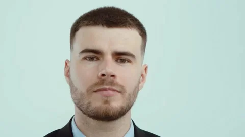 Handsome young man looking at camera and smiling while standing against grey. Stock Footage 242097623
