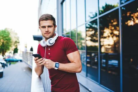 Handsome young man looking at camera while standing with smartphone Stock Photos