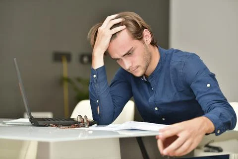 Handsome young man looking closely to some bills on a table next to a laptop Stock Photos