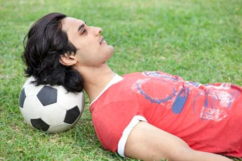Handsome young man lying on back with head on soccer ball Stock Photos