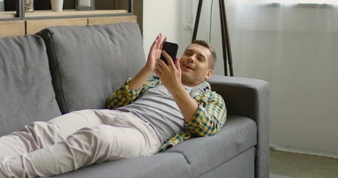 Handsome young man lying on a couch and having a video chat with his girlfriend Stock Footage 113616487