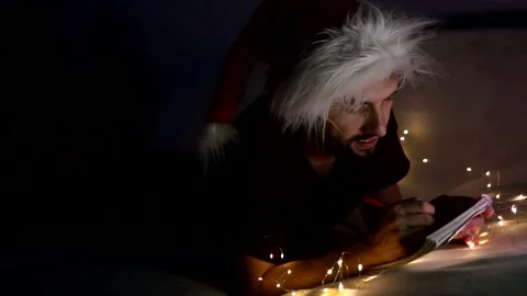 Handsome young man lying on the couch wearing santa hat, using his phone and Stock Footage 144055076