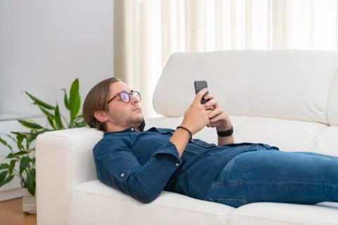 A handsome young man lying on a sofa and focused on his phone. Communication  Stock Photos