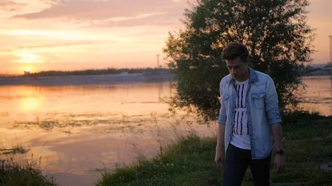 Handsome young man model posing on the lake at sunset Video stock 72838917
