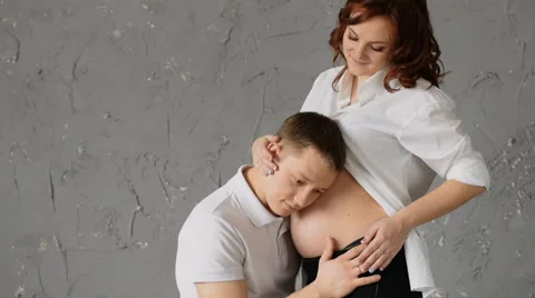 A handsome young man nuzzles the belly of his pregnant wife. Young wife pats him Stock Footage 61736450