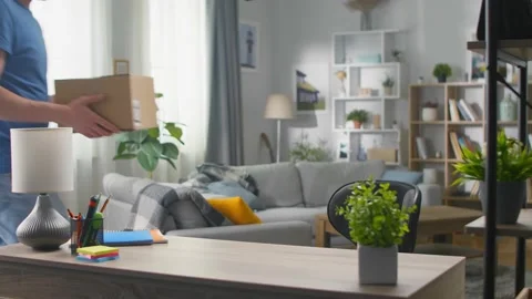A handsome young man opens a parcel while sitting at a table in the living room Vidéo 133565247