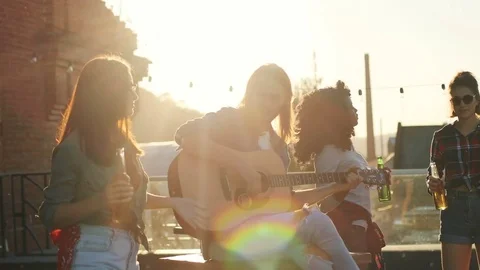 Handsome young man playing on the guitar and singing among his friends on the Stock Footage 81802366