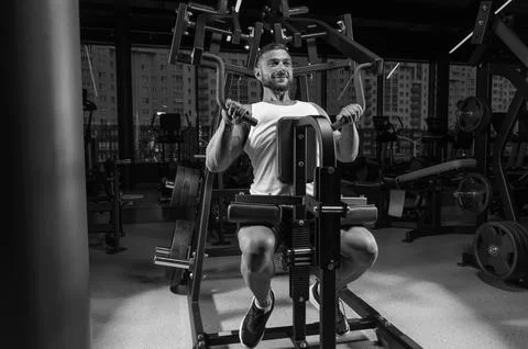 Handsome young man pumps his shoulders in a special machine. Fitness and bo.. Stock Photos
