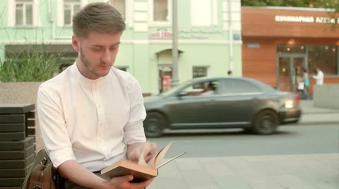 Handsome young man reading book outdoors. Man   in city urban scene. Stock Footage 66456316