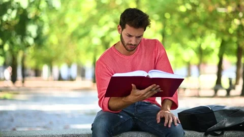 Handsome young man reading book on bench in the park Vídeos de archivo 242840265