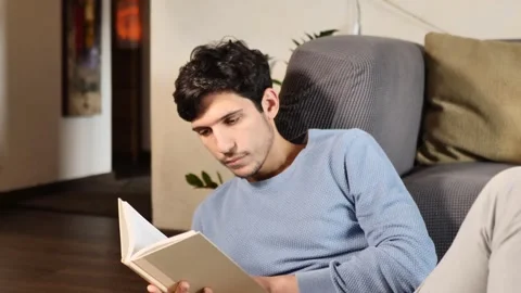 Handsome young man reading book at home in his living-room Stock Footage 242864588