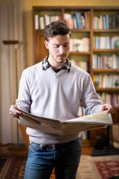 Handsome young man reading newspaper at home Stock Photos