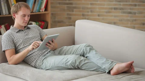 Handsome young man relaxing on couch using touchpad and smiling Stock Footage 34279611