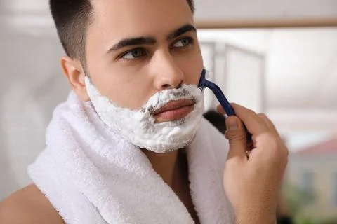 Handsome young man shaving with razor in bathroom, closeup Stock Photos