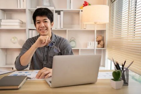 Handsome young man sits working at a desk with a laptop and office equipment, Stock Photos