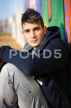 Handsome young man sitting against colorful graffiti Stock Photos