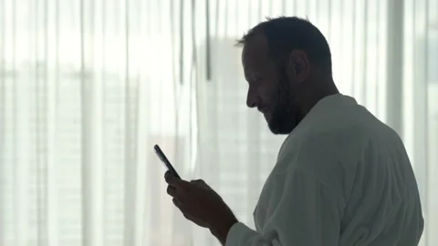 Handsome, young man sitting in bathrobe with smartphone in bedroom Stock Footage 86536118