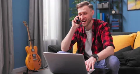 A handsome young man is sitting on couch talking on the phone at living room. A 動画素材 153893528
