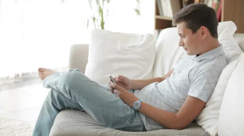 Handsome young man sitting on sofa using mobile telephone and smiling Stock Footage 27302957