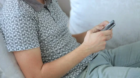 Handsome young man sitting on sofa and using mobile phone. Panning camera Stock Footage 34279583