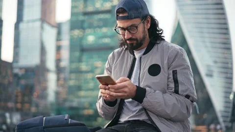 Handsome young man sitting on the street with a smartphone in hands Stock Footage 141898853