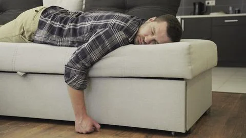 Handsome young man sleeping on the couch in his living room at home. Slow motion Stock Photos