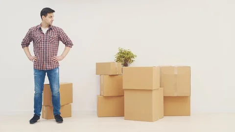 Handsome young man standing keeping hands akimbo, pointing at the pile of boxes. Stock Footage 120069442
