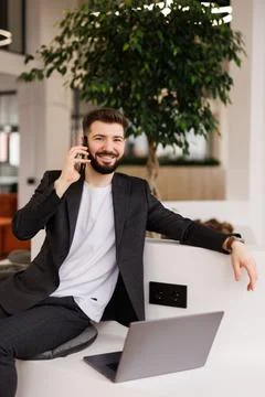 Handsome young man talking on smart phone and using computer while working .. Stock Photos