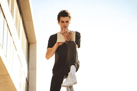 Handsome young man using digital tablet while sitting on railing against clear Stock Photos