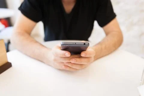 Handsome, young man using his mobile phone in a public area, at the table Stock Photos